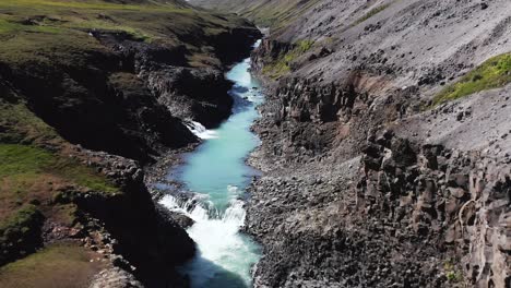 Rising-from-Studlagil-gorge-with-magical-blue-Icelandic-water,-aerial
