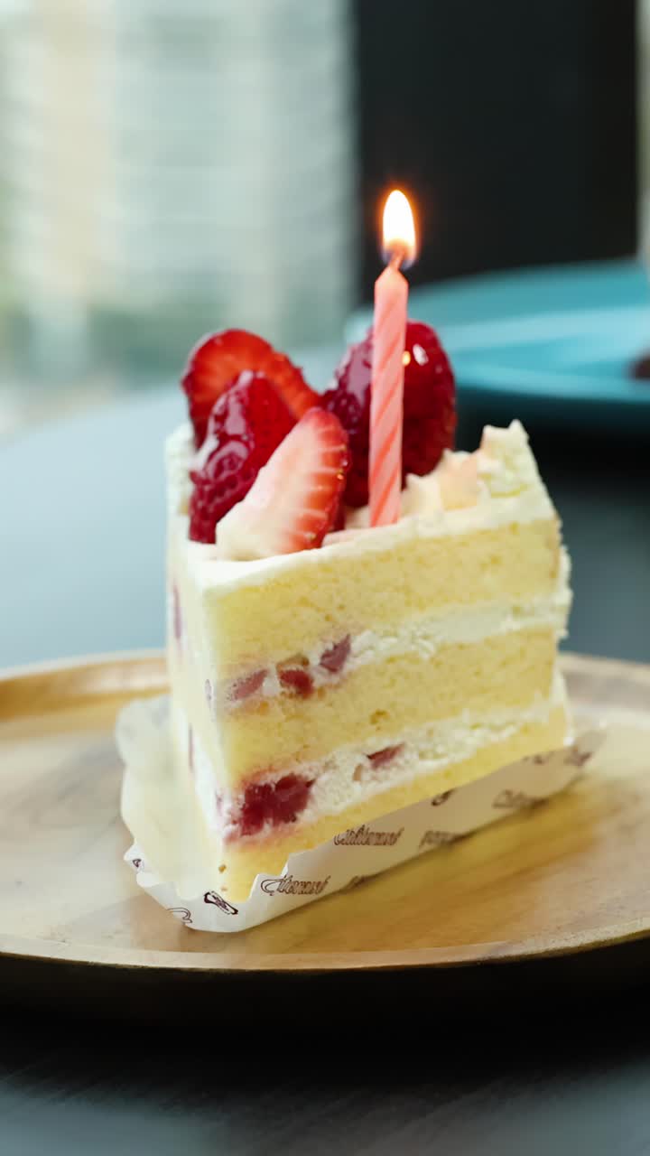 自然光の下、いちごショートケーキ一切れに置かれたピンクのろうそくに手が火をつけるクローズアップ、浅い被写界深度