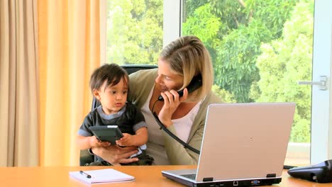 young mother holding baby while working in office