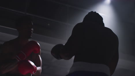 toma de cerca de dos boxeadores masculinos con guantes en el ring de boxeo luchando en un partido de boxe o con una iluminación de bajo nivel.