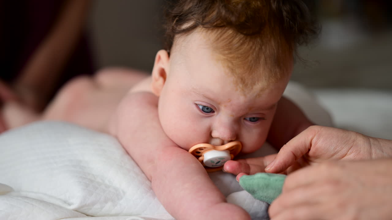 Cute baby lying on stomach during tummy time while interacting with a pacifier