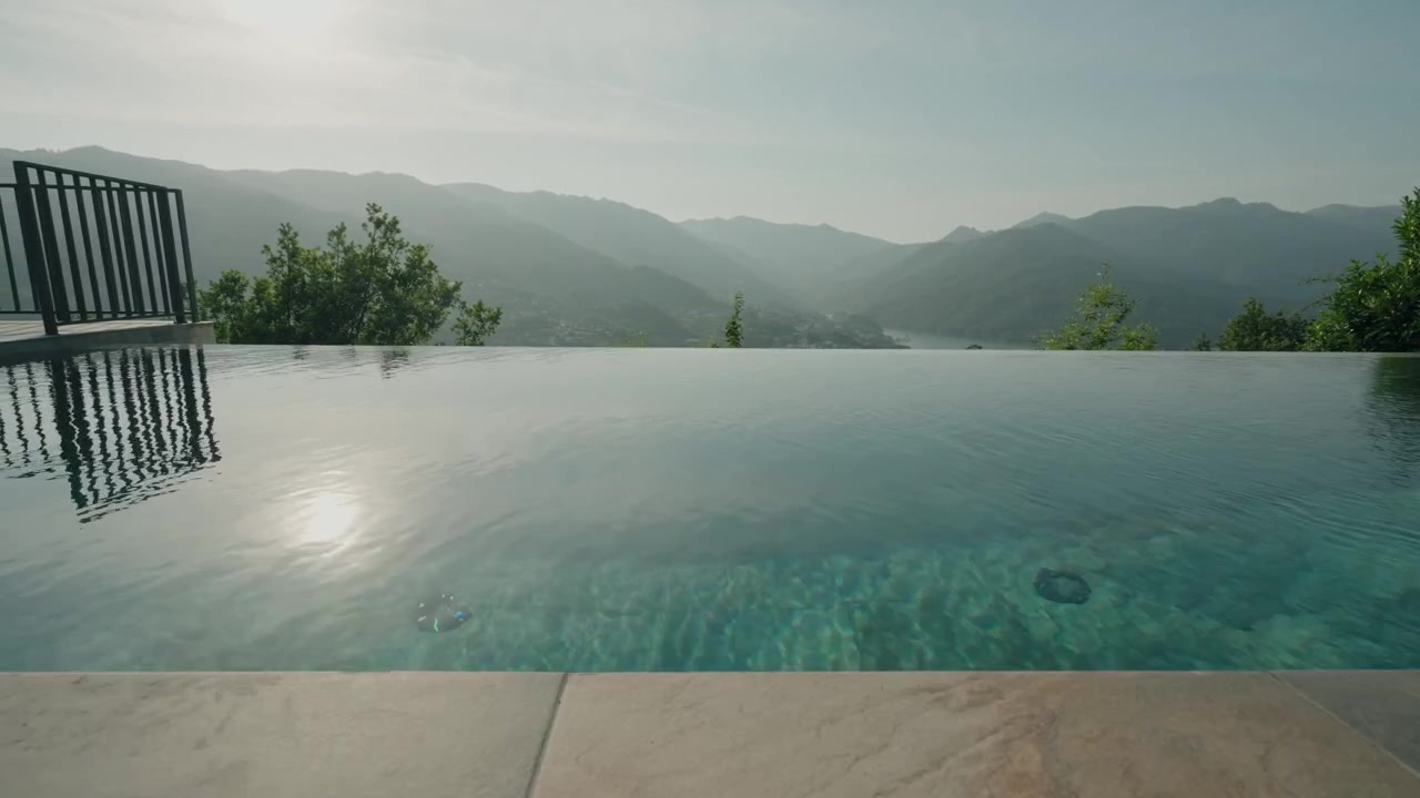 Infinity-Pool-Wasser mit sich ausbreitendem Wellenring und Blick auf dunstige Berge und ein Flusstal.