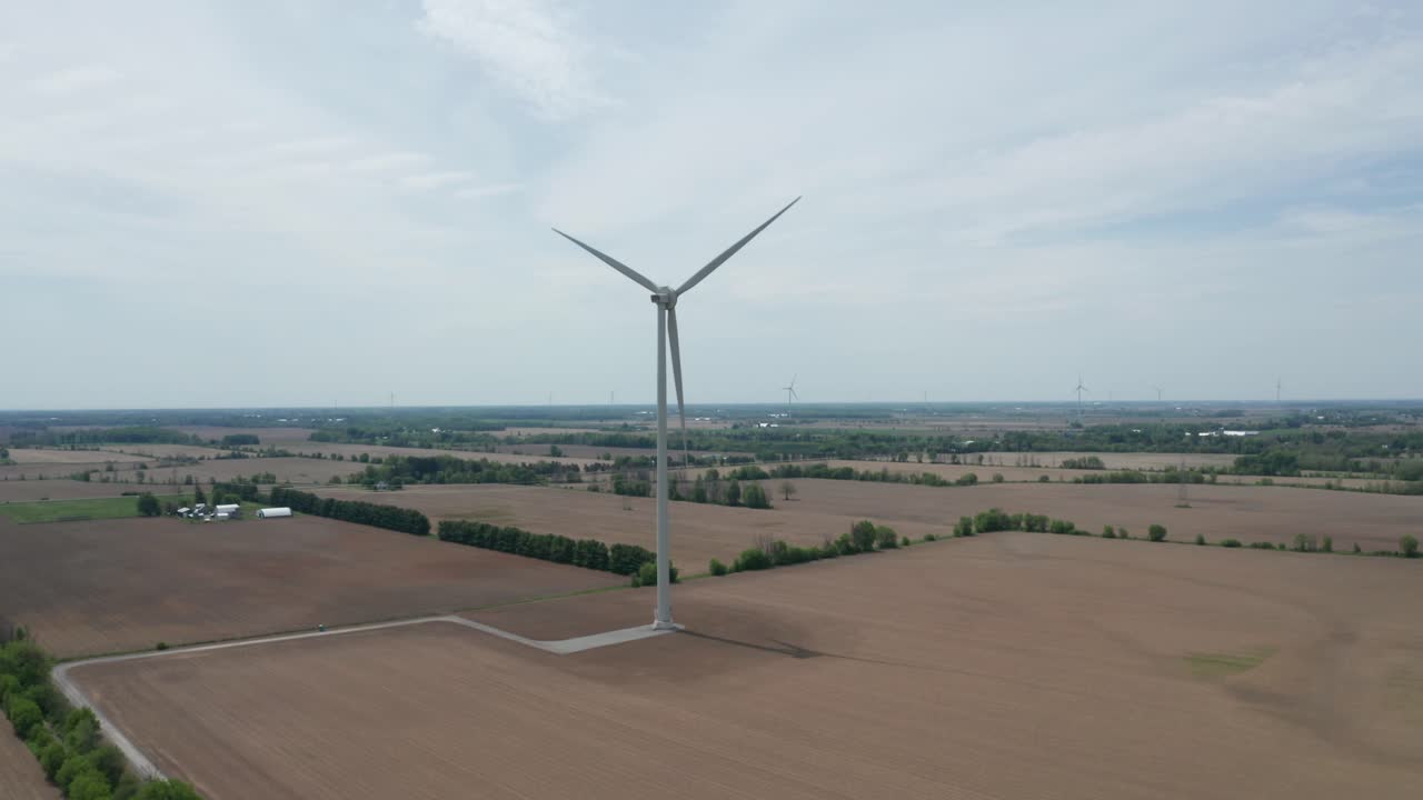 Aerial view from drone approaching spinning blades of massive wind power generation tower