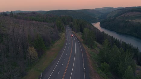drone shot of emergency fire vehicle driving on highway next to river during sunset