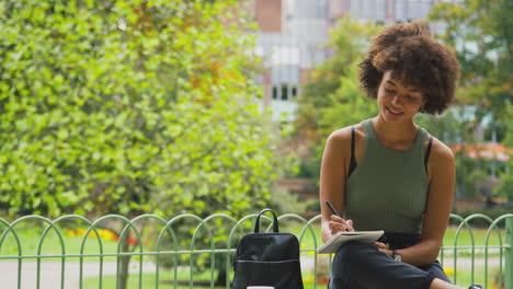 jeune femme à l'extérieur dans le parc assise sur un banc travaillant à écrire dans un carnet