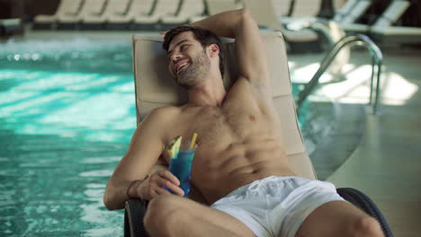 retrato de un hombre bebiendo un cóctel cerca de la piscina. un tipo sexy coqueteando en una tumbona.