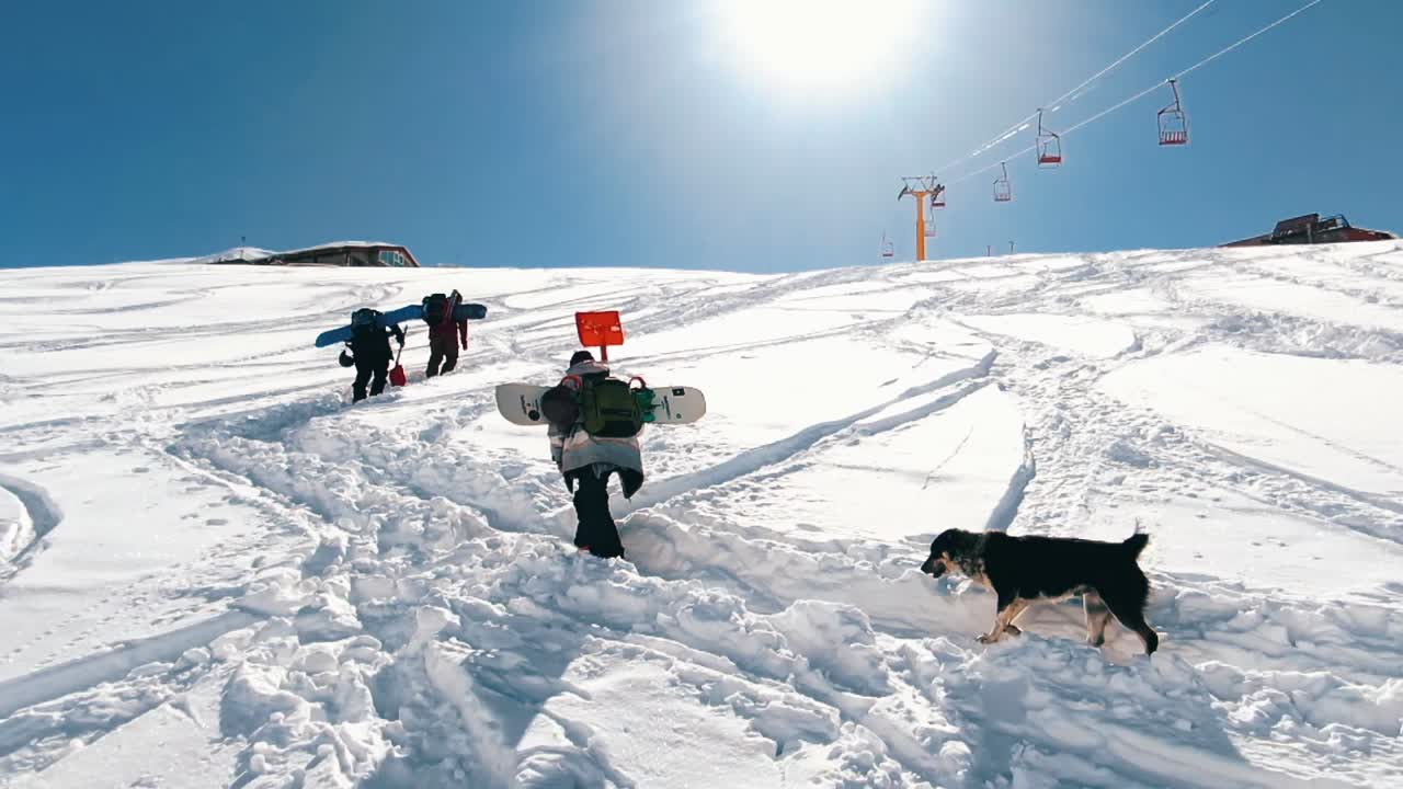 slow motion: Snow boarders walking up the mountain. Camera moving slowly behind group of snowboarder walking up the mountain