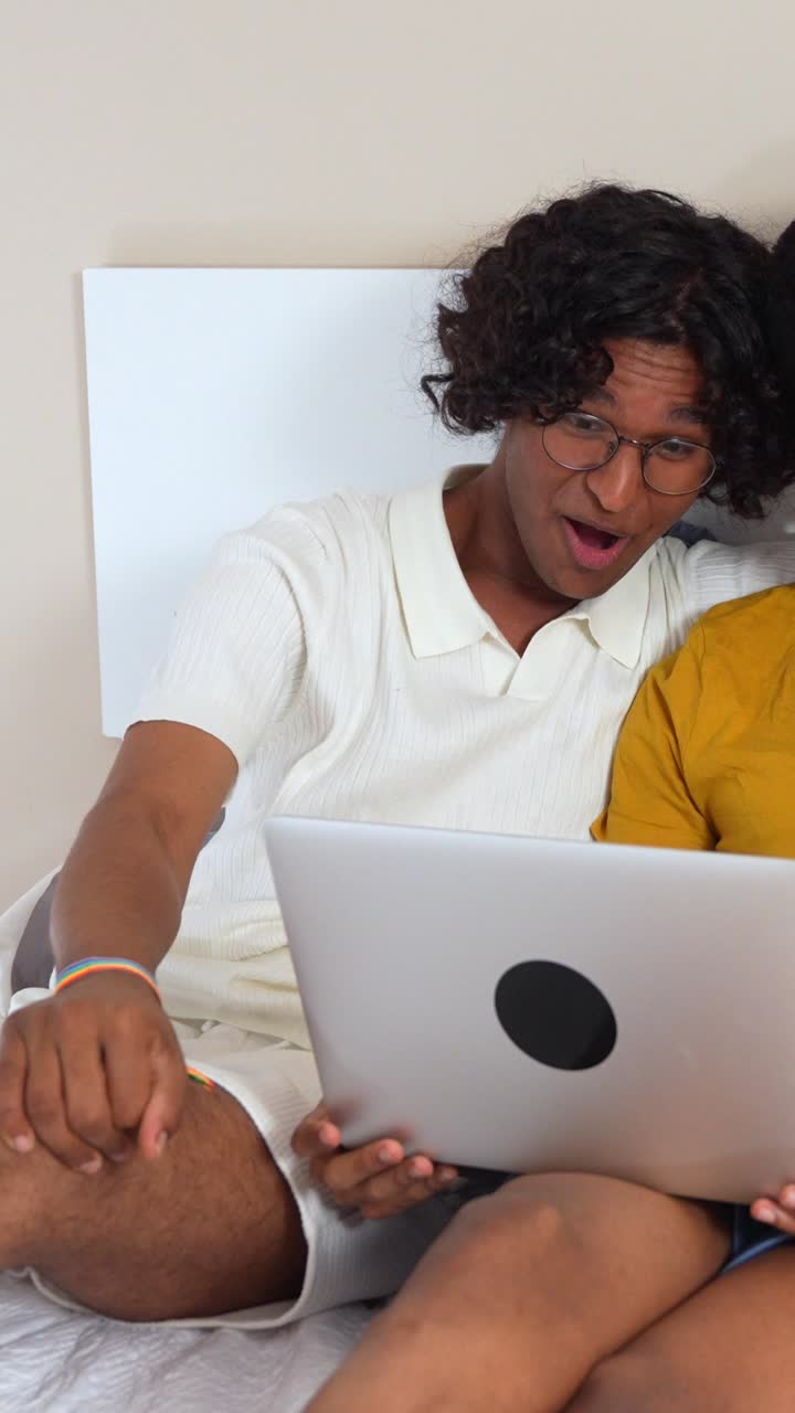 Two LGBTQ individuals smiling while using a laptop indoors