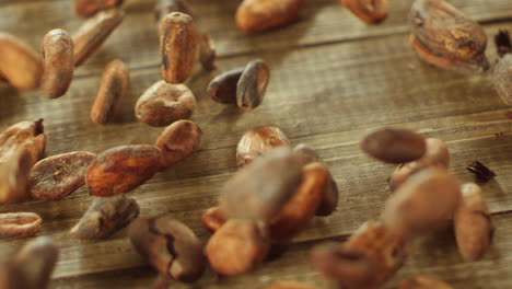 raw cocoa beans falling on wooden table surface in slow motion.