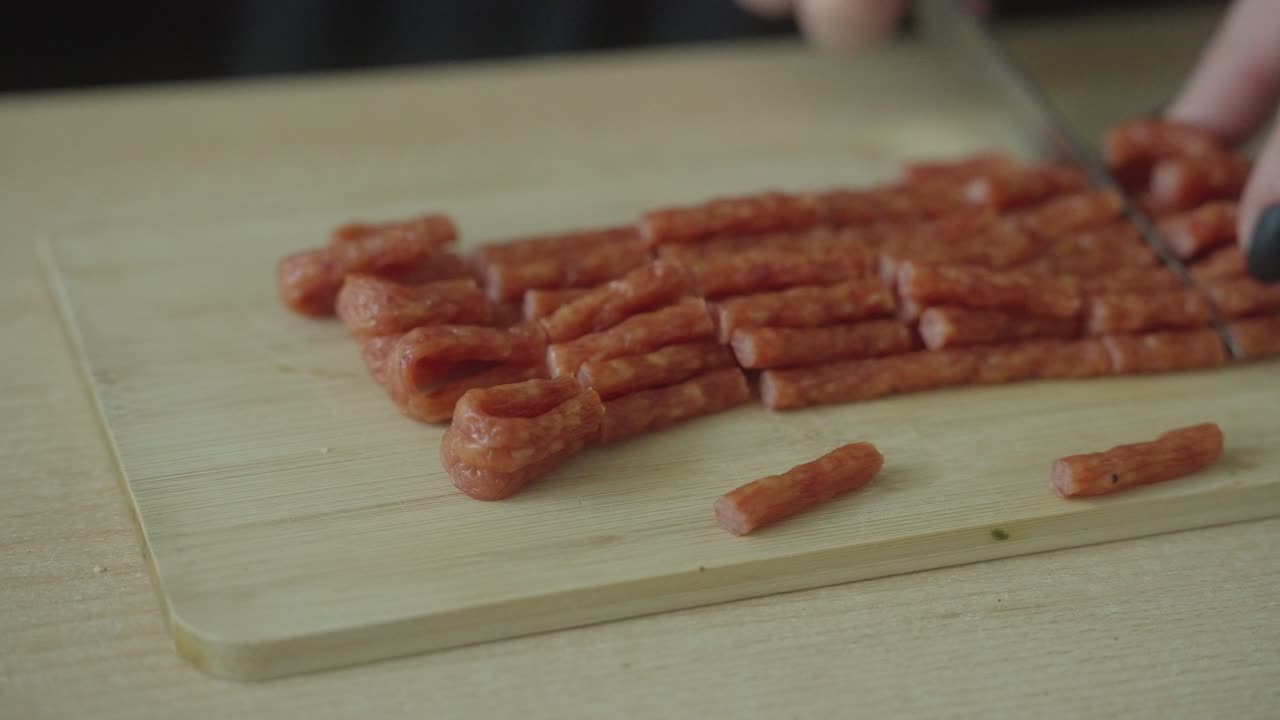 Woman slicing thin kabanos on a wooden cutting board. Meat delicacy prepared at home