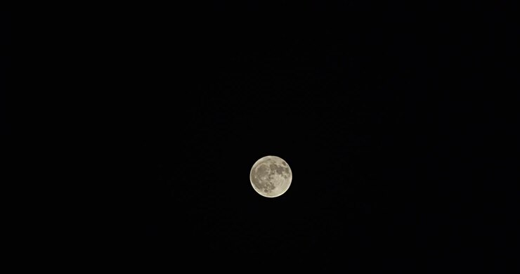 Plano amplo em time-lapse de uma lua cheia com névoa passageira, subindo do canto inferior esquerdo para o canto superior direito.