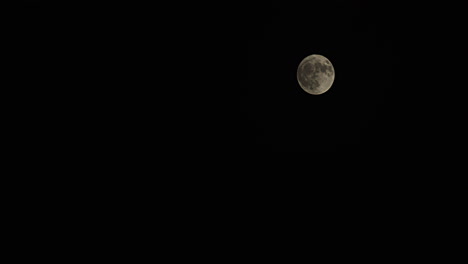 Time-lapse-wide-shot-of-a-full-moon-with-passing-fog-as-it-rises-from-the-lower-left-to-the-upper-right