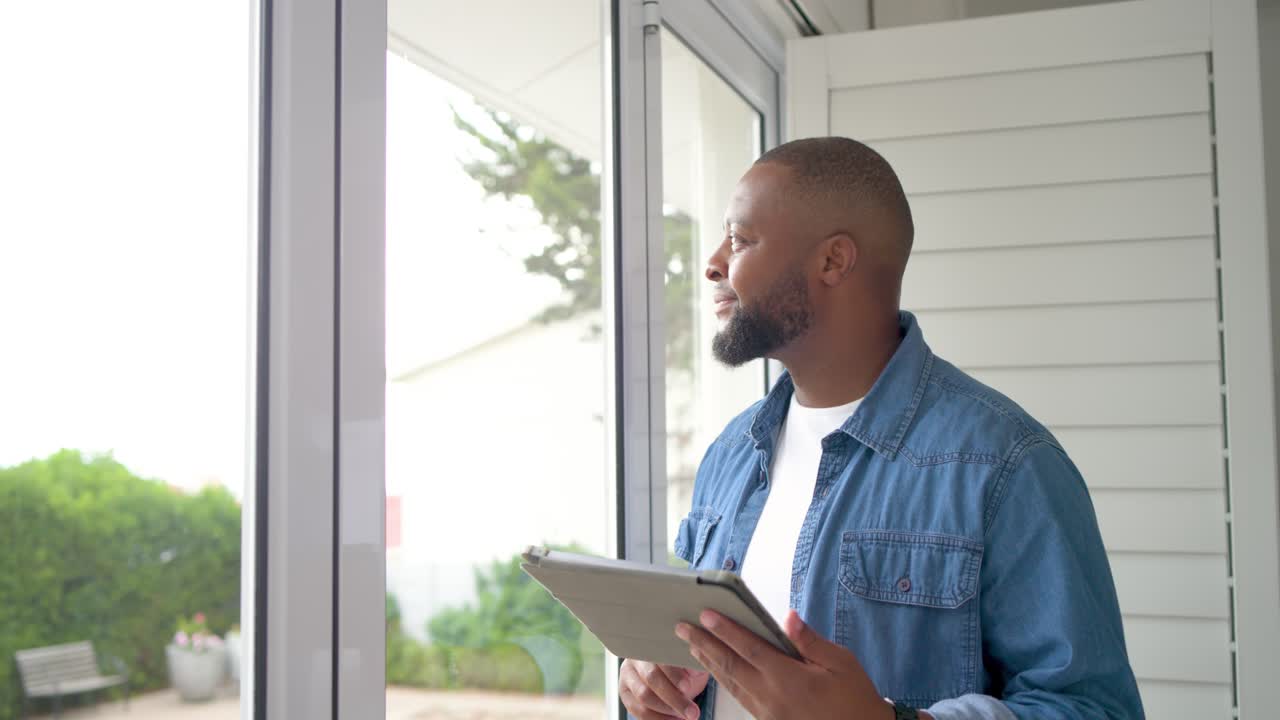African American man using tablet at door tapping, swiping, glancing and thinking in denim