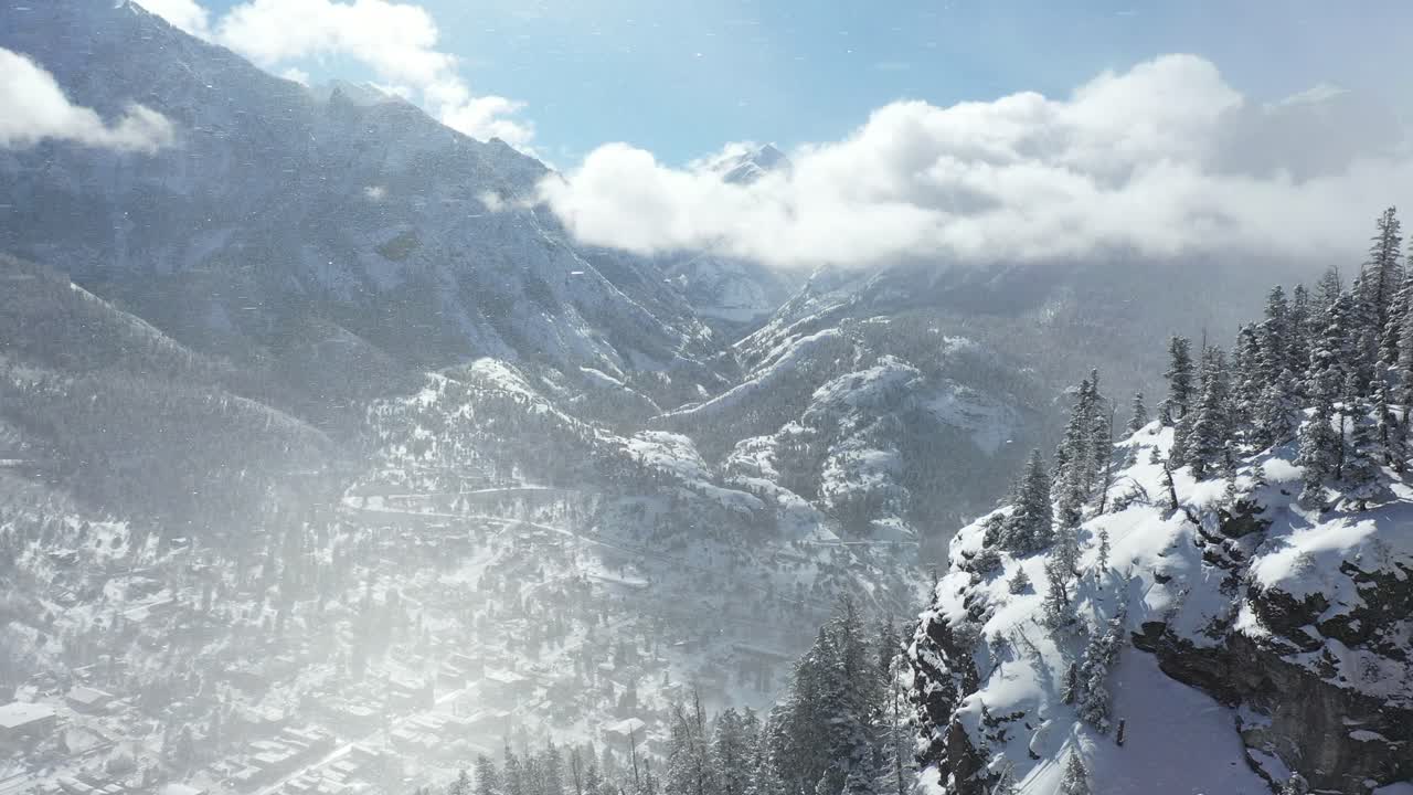 Aerial view, snowfall and wind above sunny valley and snow capped hills on cold winter day, Ouray, Colorado USA, dramatic drone shot