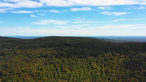 Aerial-drone-shot-over-the-top-of-colorful-autumn-trees-pushing-in-towards-a-small-mountain-peak-as-summer-ends-and-the-season-changes-to-fall-in-Maine