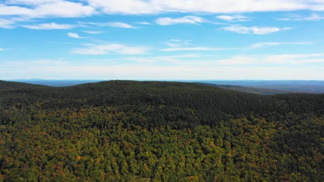 aerial drone shot over the top of colorful autumn trees pushing in towards a small mountain peak as summer ends and the season changes to fall in maine