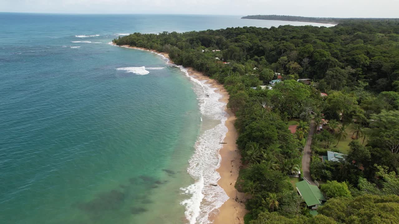 vuelo sobre una playa paradisiaca con agua turquesa bordeada por una selva con algunas chozas