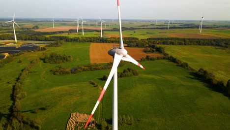 Toma-Aérea-De-Las-Turbinas-Eólicas-Que-Funcionan-En-Un-Parque-Eólico-Que-Genera-Energía-Eléctrica-Verde-En-Un-Amplio-Campo-Verde-En-Un-Día-Soleado,-Uso-De-Recursos-Renovables-De-Energía,-Paralaje,-4k