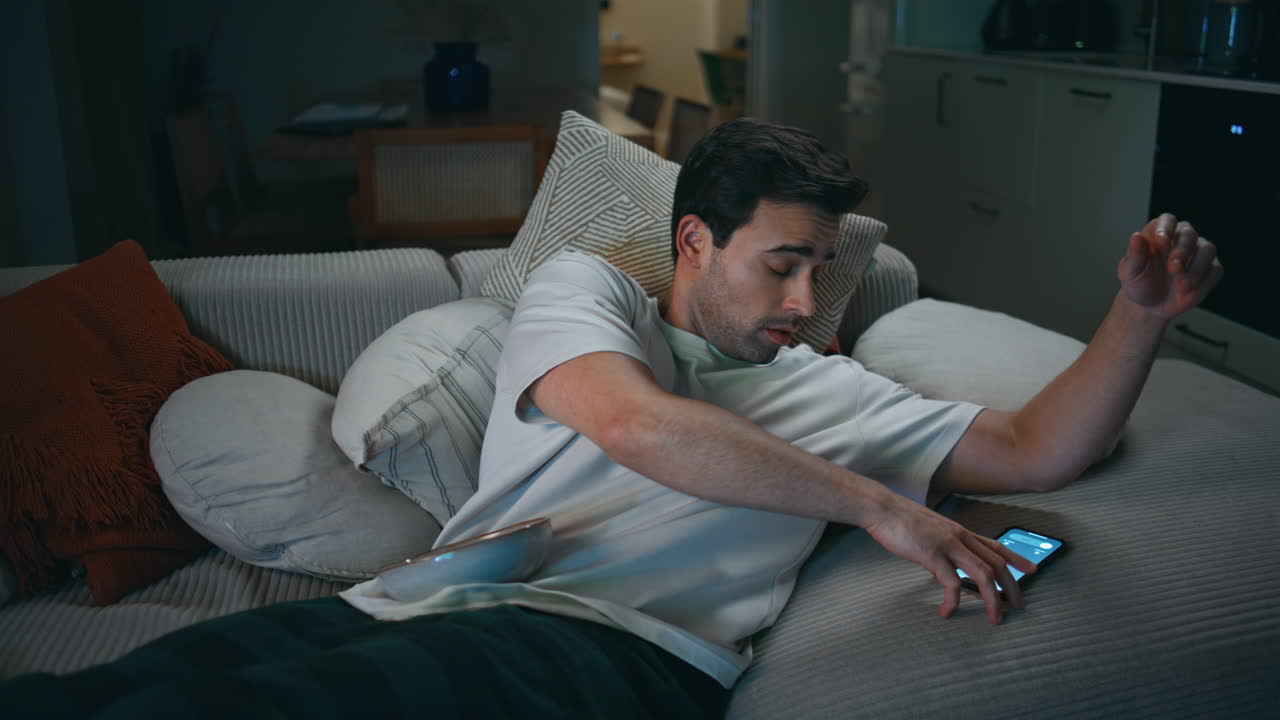 Resting man answering call at smartphone lying home sofa closeup. Sleepy guy