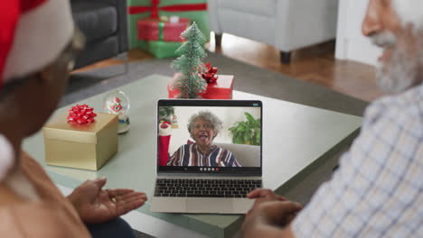 Happy-african-american-senior-couple-on-laptop-video-call-with-female-friend-at-christmas-time