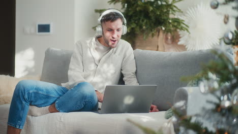 man puts on headphones and does online shopping on laptop during christmas