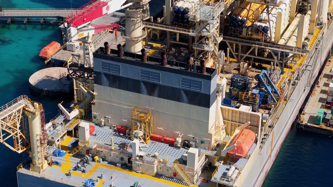 Aerial overview of complex marine machinery of oil platform drilling rig ship with workers and machinery on deck, surrounded by deep blue waters