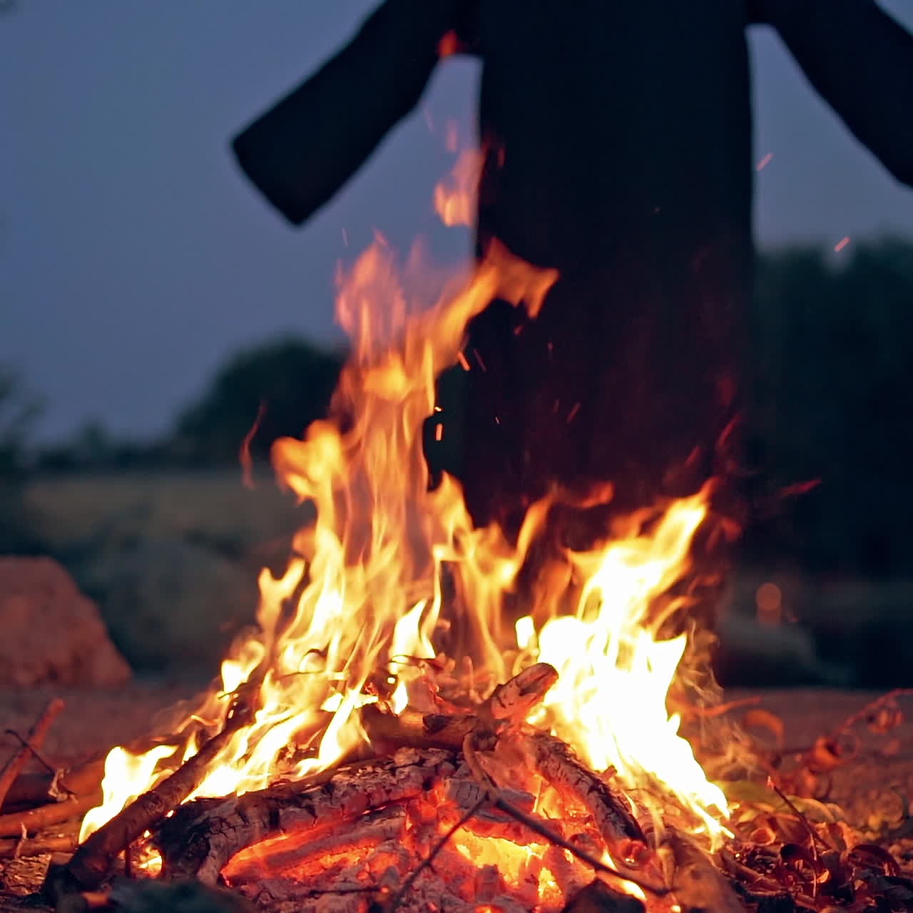 Bright campfire and black costume without hands behind. Fire and witch in nature in the evening. Slow motion.