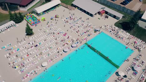 Vuelo-Aéreo-Sobre-La-Playa-Mucha-Gente-Está-Tomando-El-Sol-Nadando-En-La-Piscina