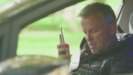 mature man sitting in broken down car calling repair shop or garage recovery service on mobile phone