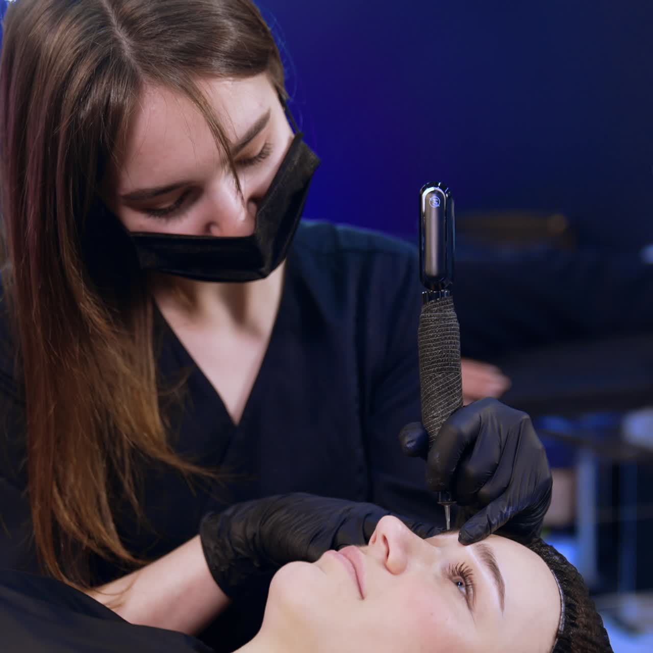 Brow-maker in black mask and gloves uses special tool for permanent make up. Client is having salon procedure on eyebrows. Close up