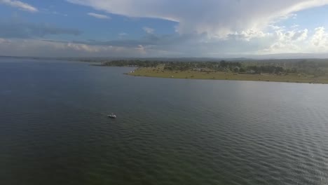 aerial drone footage of a big storm cloud over a small town near a lake with mountains in the background and a boat sailing