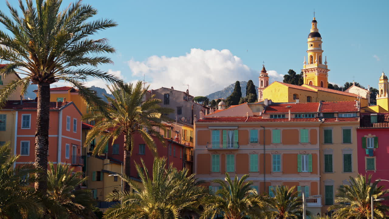 Distant view of the St Michel Basilica surrounded by colourful buildings and palm trees, Menton, France