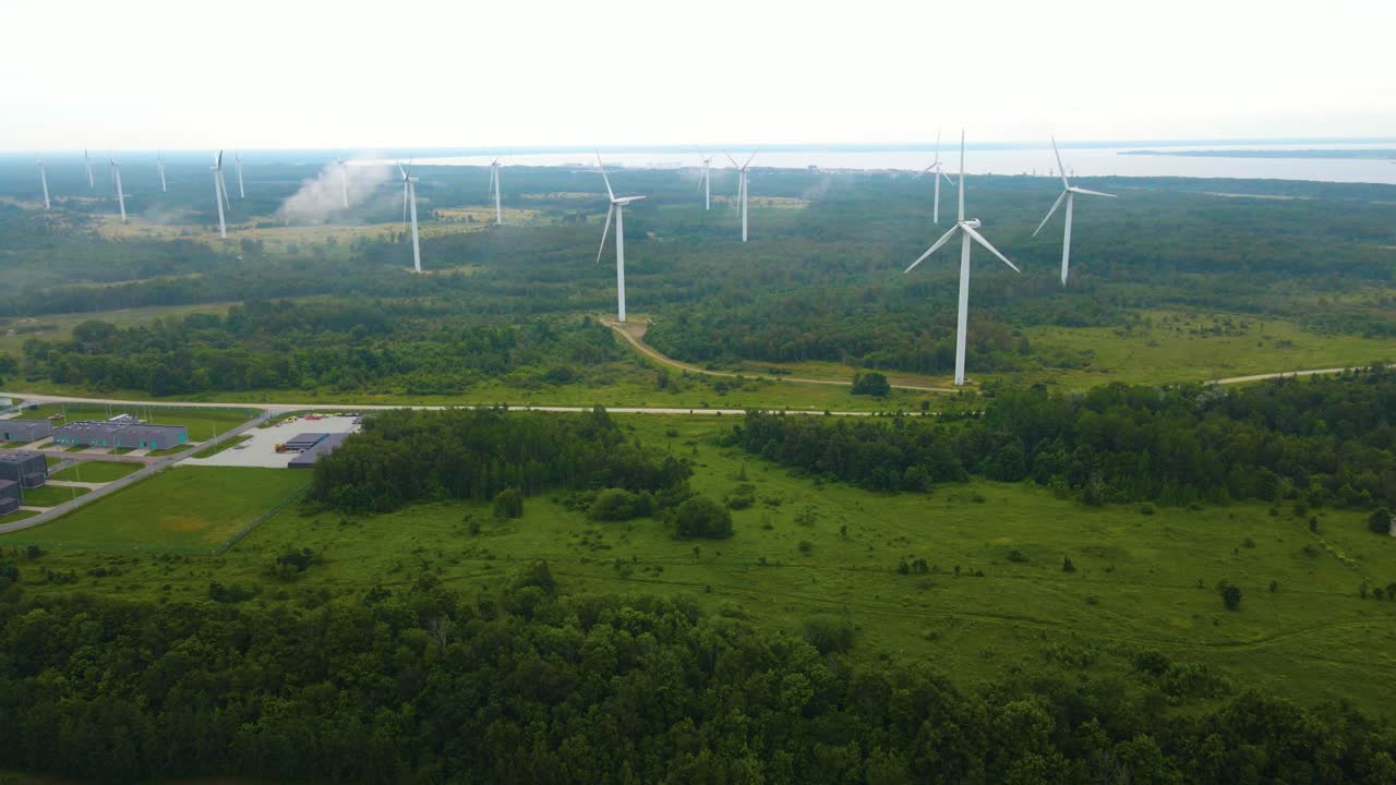 Aerial drone video revealing a large misty and foggy peninsula with smoke clouds where large green energy production wind turbines are spinning and rotating with ocean sea water visible in the back