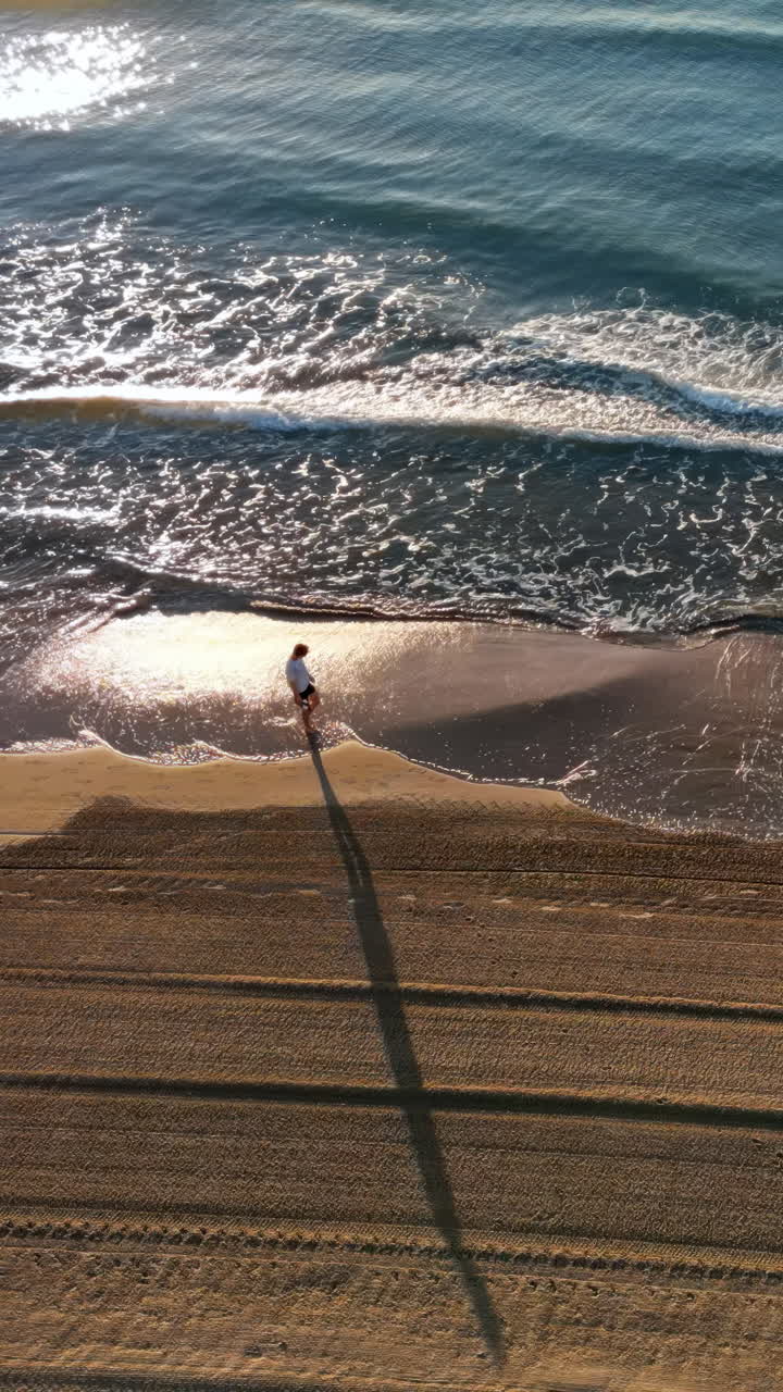 Man walking on the beach with waves hitting the shore in Alicante, Spain. Vertical