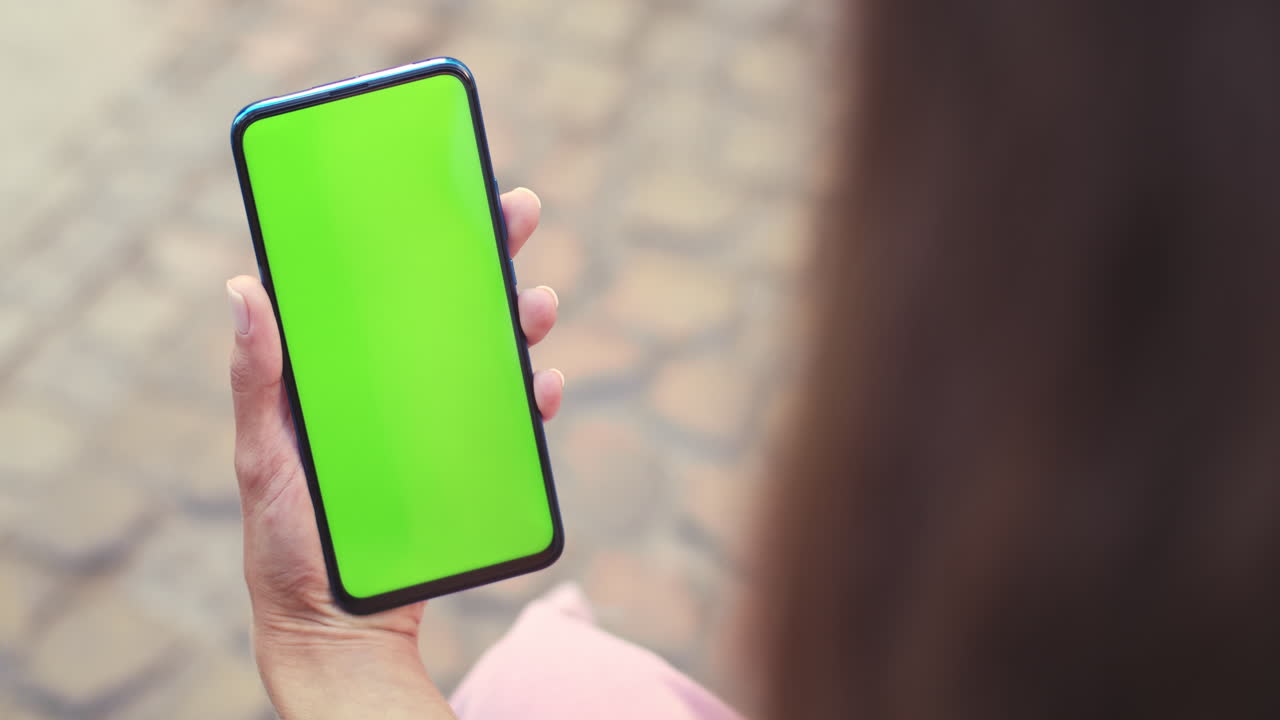 Person holding a smartphone with a green screen display