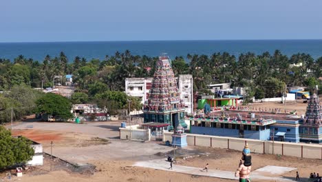 a hindu temple complex with ornate spires stands near the chennai shoreline. lush palm trees surround the colorful architecture against a backdrop of the ocean