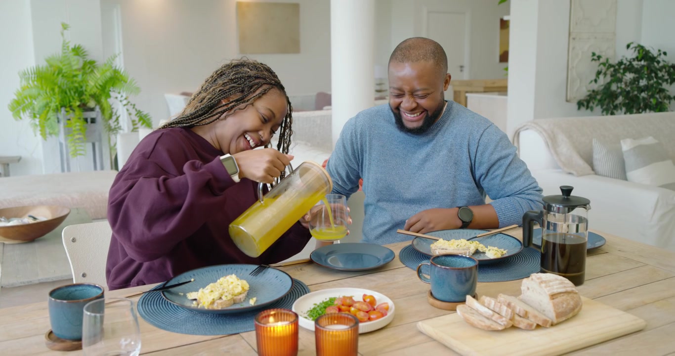 African American couple at home, woman lifting pitcher, pouring juice, man steadying glass for meal