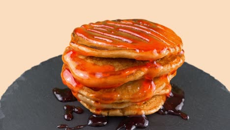 pancakes with strawberry topping. pancake lies on a black slate round stone. pink background.