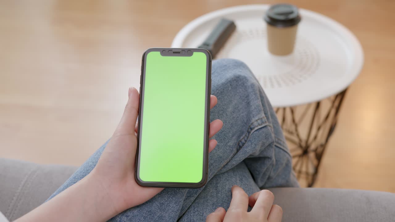 mujer sosteniendo una maqueta de pantalla verde de teléfono inteligente con un mensaje de tipo en el sofá en casa.
