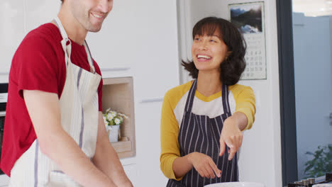 Video-of-happy-diverse-couple-baking-together-in-kitchen