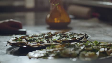 Pizza-maker-spreading-parsley-over-pizza-in-kitchen