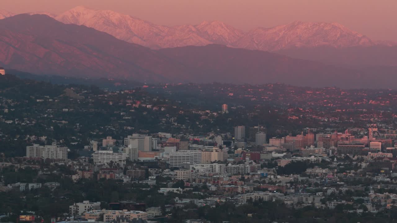 Inquadratura dolly aerea con teleobiettivo di Hollywood con montagne innevate sullo sfondo durante l'ora magica a Los Angeles, California. 4K.