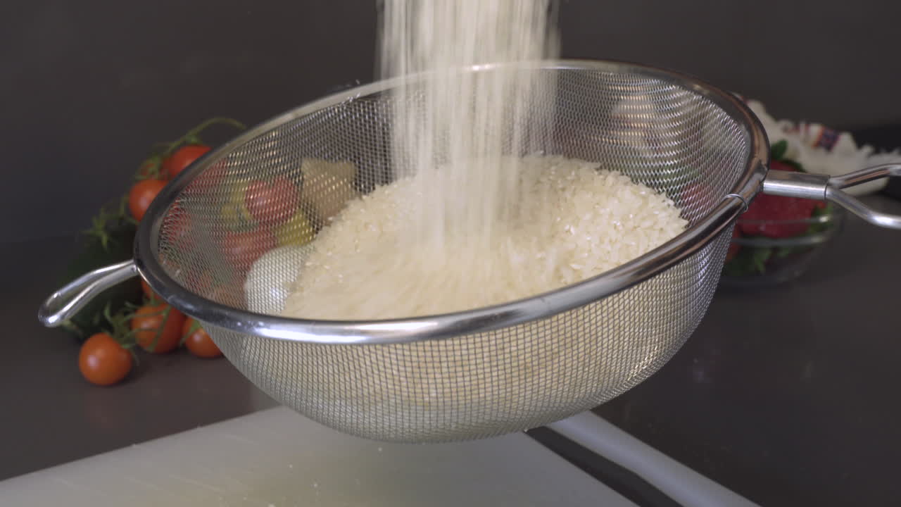 Sifting Uncooked Rice Grains In A Stainless Sieve Over The Chopping Board In The Kitchen - closeup shot