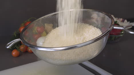 sifting uncooked rice grains in a stainless sieve over the chopping board in the kitchen - closeup shot
