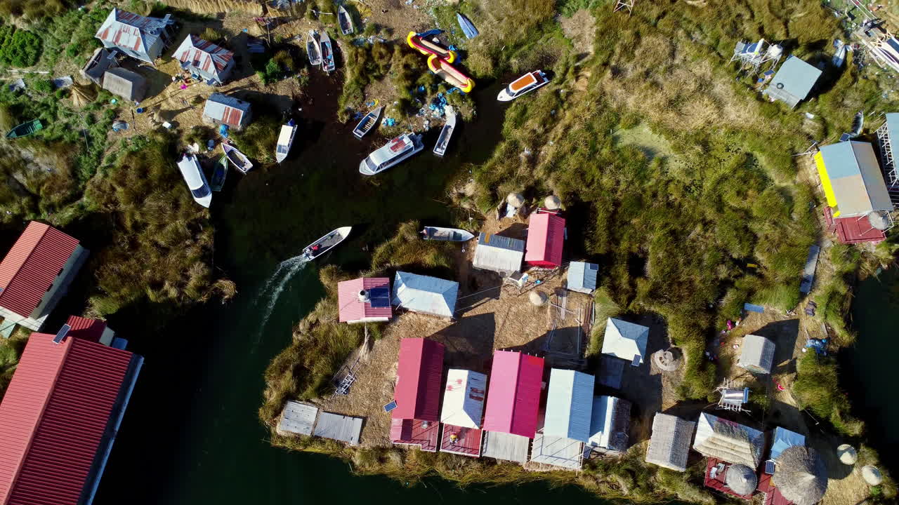 drone de arriba hacia abajo se eleva sobre la isla de uros casas flotantes en el lago titicaca con barcos atracados
