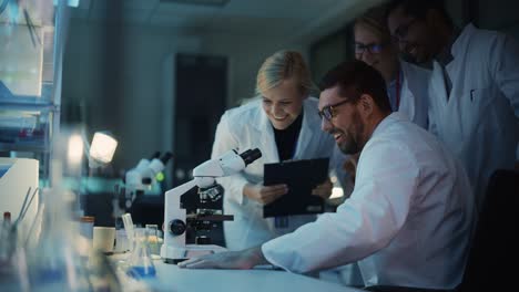 surprized male reseach scientist makes an important discovery while researching samples under the microscope. happy colleagues give high five and share success with fellow bioengineers.