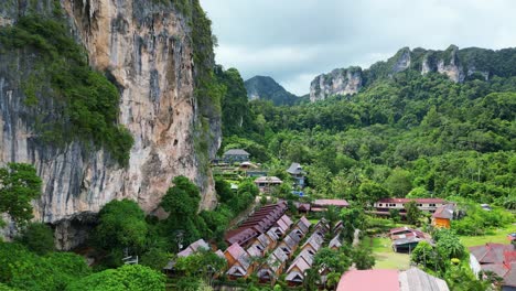 a lush landscape featuring a cluster of tropical lodges surrounded by towering cliffs and dense greenery.
