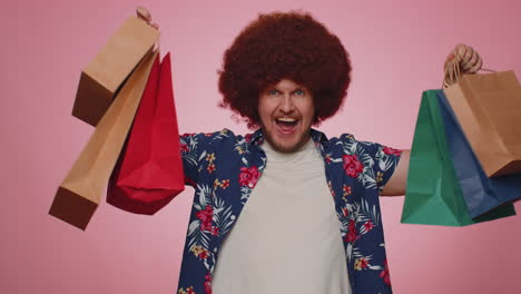 hombre turista feliz mostrando bolsas de compras, promocionando descuentos de vacaciones, asombrado por los bajos precios