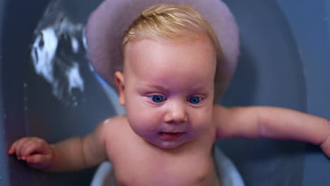 sweet little blond blue-eyed baby in a bath. close up portrait of a child enjoying bathing. top view.