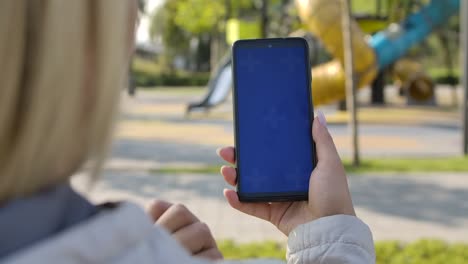 behind shoulder view of a woman holding a smartphone with a screen with a chroma key, browsing content touching or swiping. browsing internet, watching content, videos, blogs. close up. slow motion